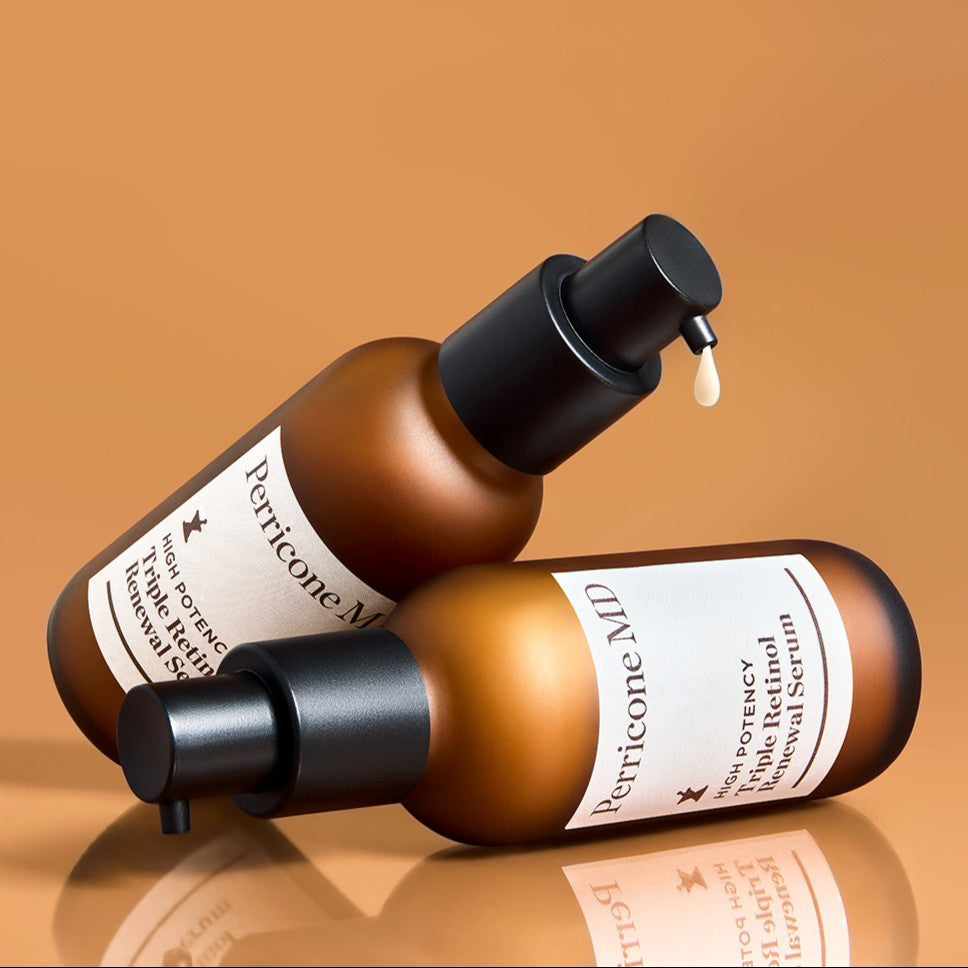Dos botes de Triple Retinol Renewal Serum, uno tumbado en una superficie reflejante y el otro apoyado encima del primero. Se ve una gota del producto que sale del segundo bote.